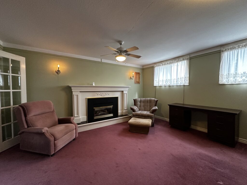 Dated lower-level family room in a backsplit home, with burgundy carpet, sage green walls and a gas fireplace.