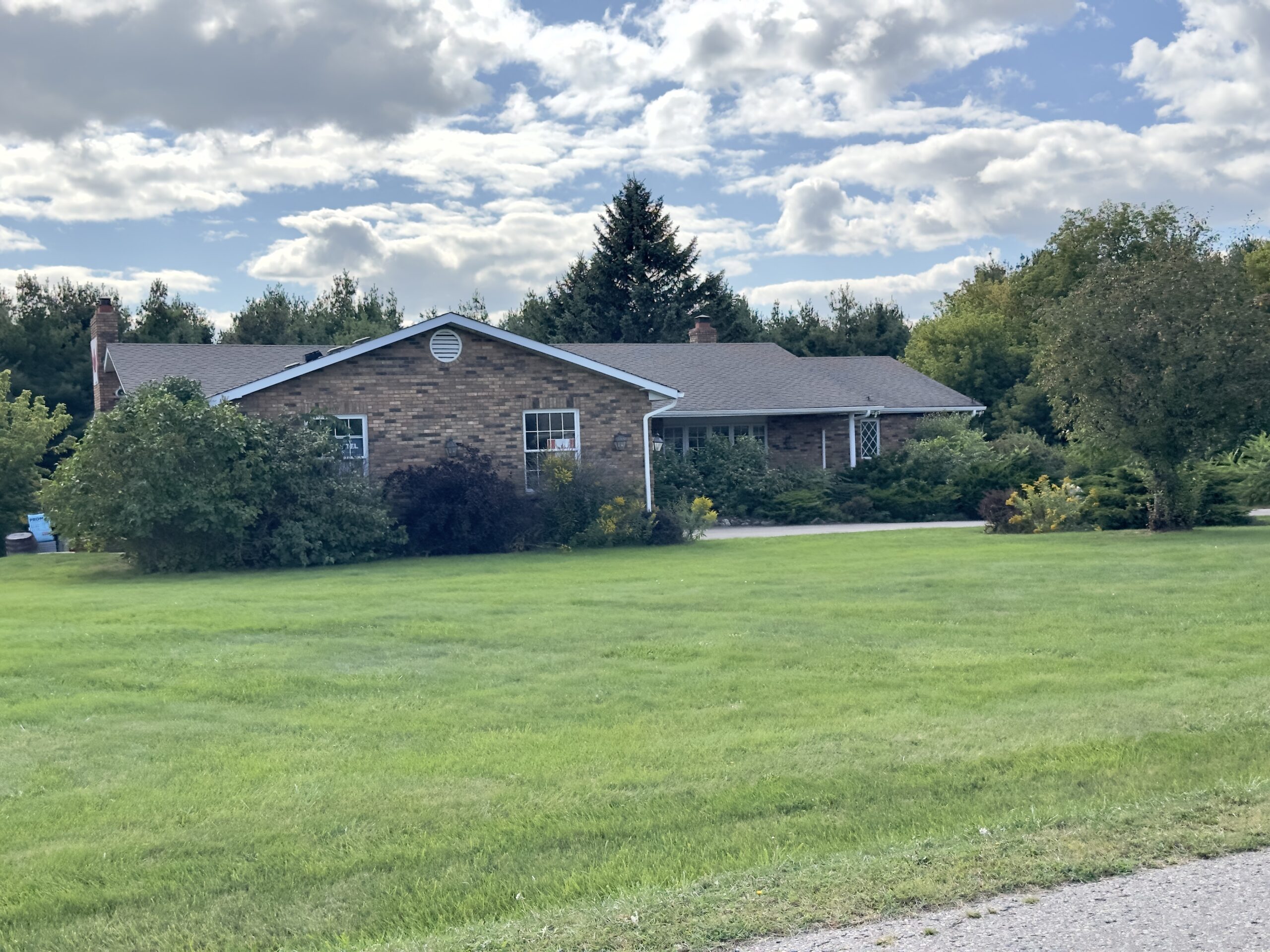 Brick bungalow set back on a large lawn with mature evergreens on a rural road in Caledon