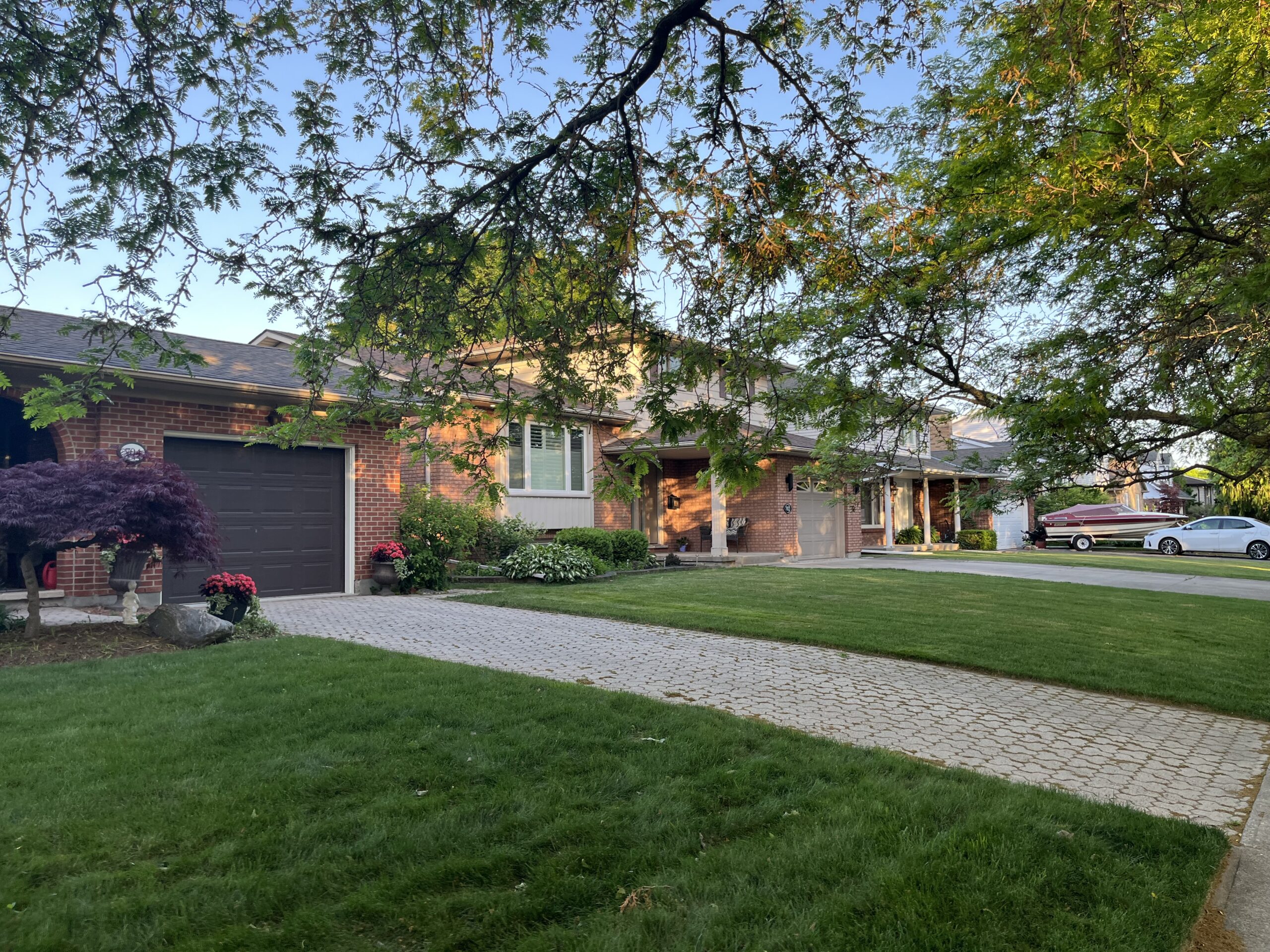Sunlit brick sidesplit with an interlocking driveway on a mature tree-lined street in St Catharines, Ontario.
